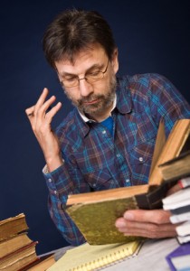 Mature man reading old book surrounded by heaps of books